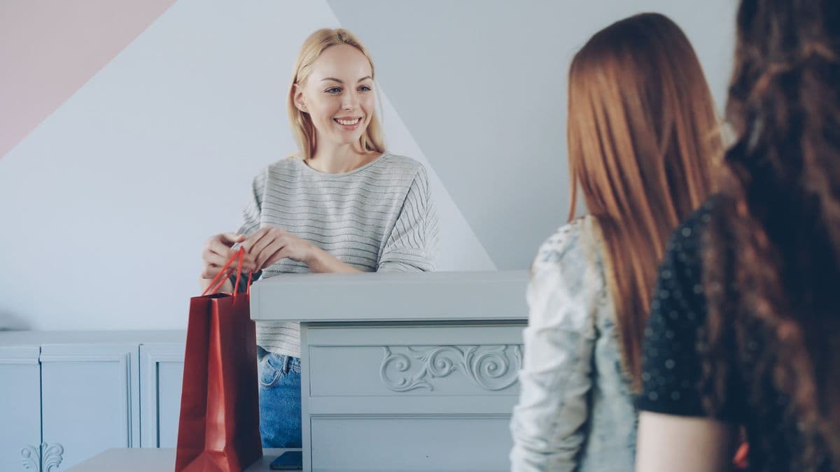 Lojista sorrindo entregando a sacola da compra para as clientes no balcão
